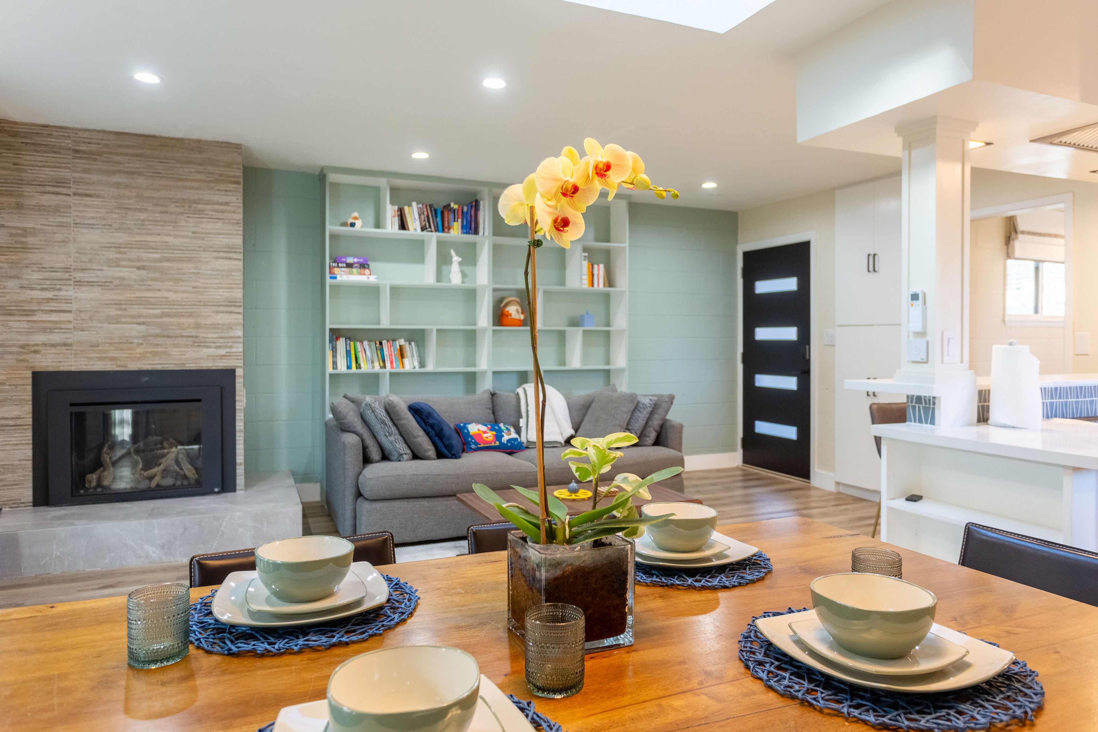 A modern living room with a dining area, a fireplace, and a bookshelf filled with books.