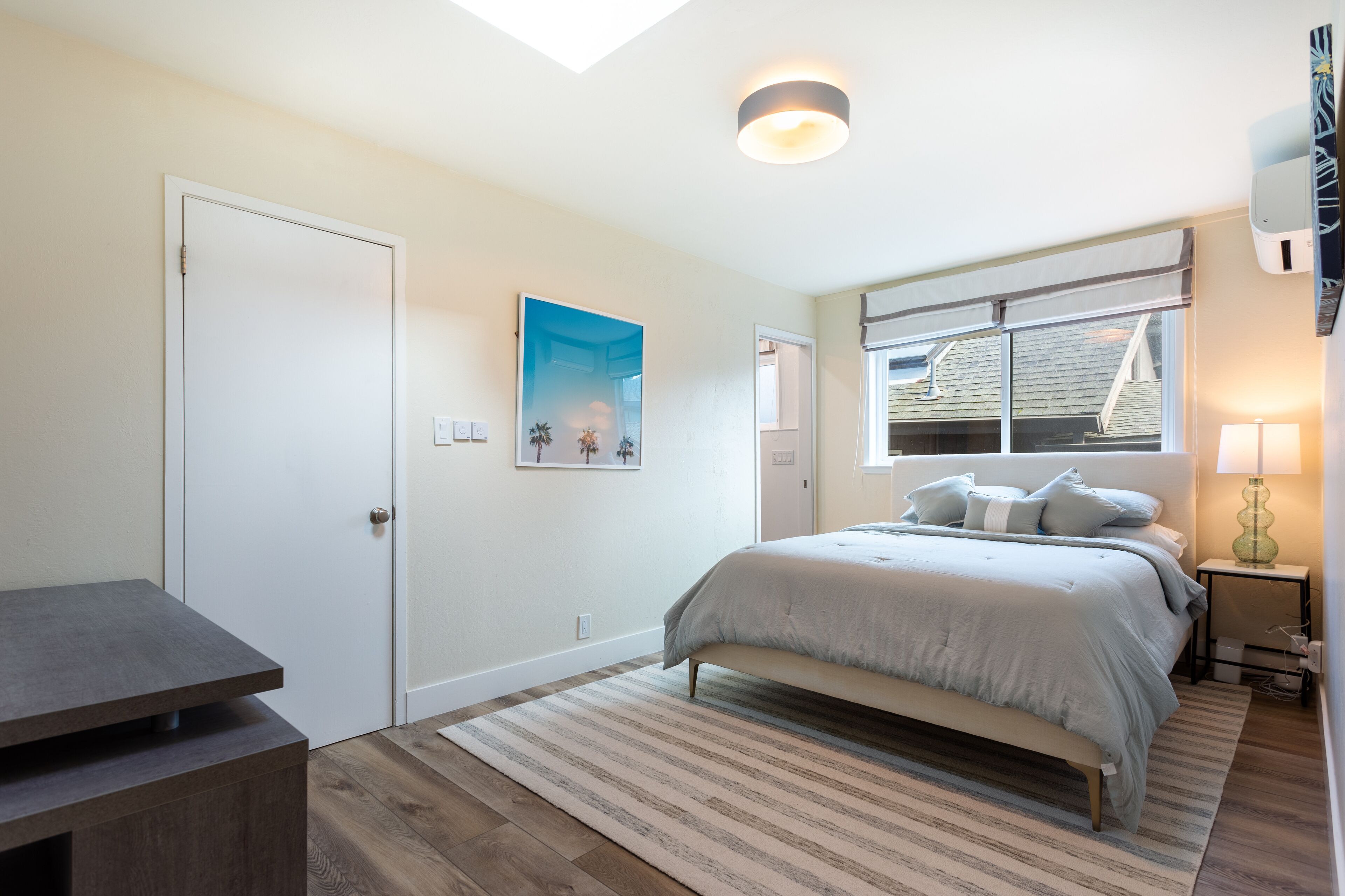 Une chambre à coucher avec un lit, une table de chevet, une lampe et une fenêtre donnant sur l’extérieur.