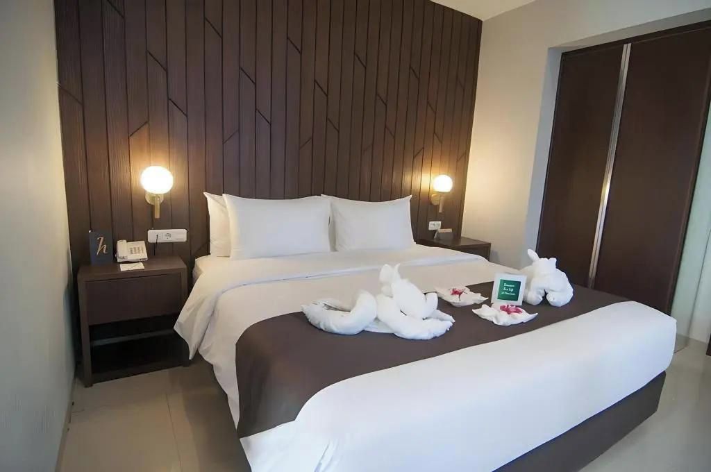 A hotel room with a bed, two bedside lamps, a telephone, and a sign indicating the room number.