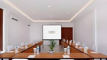 A conference room with a long table, chairs, a projector screen, and a potted plant.