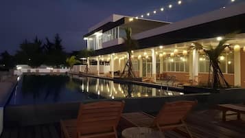 A modern hotel with a swimming pool, wooden deck chairs, and string lights.