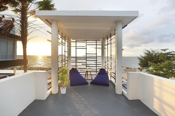 A balcony with a view of the sea, featuring a white railing, two blue cushions, and a small table.