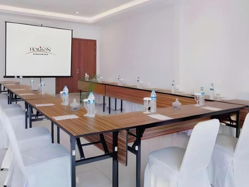 A conference room with a long table, white chairs, a projector screen, and a wooden partition.