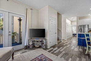 A spacious living room with a flat-screen TV, a staircase, and a kitchen area.