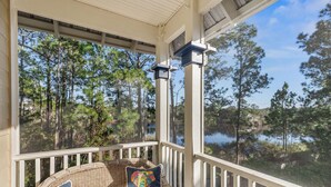 A covered porch with wicker furniture and pillows, overlooking a forest and a body of water.