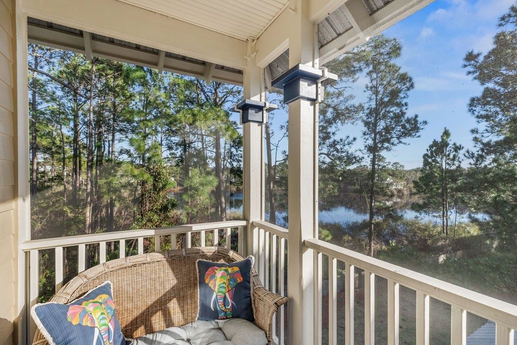 A covered porch with wicker furniture and cushions, overlooking a forest and a body of water.