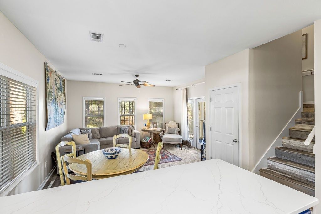 A spacious living room with a dining area, a ceiling fan, and a staircase leading to another level.