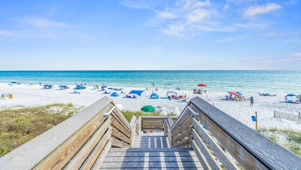 A wooden staircase leading to a beach with umbrellas and beach chairs.