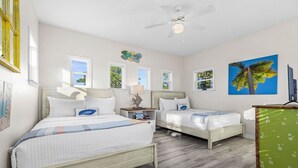 A bedroom with two beds, a ceiling fan, and a painting of a palm tree.