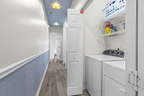 A laundry room with a washing machine, a dryer, and shelves with laundry supplies.