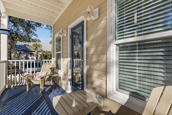 A covered porch with a table and chairs, a blue door, and a window with blinds.