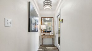 A hallway with a wooden floor, a desk with a lamp, and a mirror on the wall.