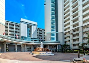 Un hotel moderno con una fontana centrale, diversi piani e cielo sereno.