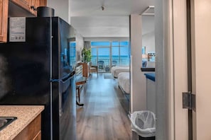 A compact hotel room with a kitchenette, a balcony with a view, and a bed.