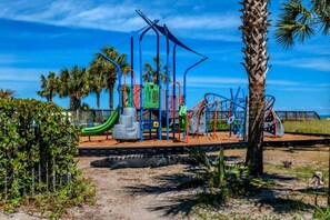A playground with various play structures, surrounded by palm trees and a clear sky.
