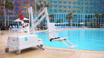 Un espace aménagé au bord de la piscine, comprenant un fauteuil élévateur pour faciliter l’accès à la piscine, des chaises longues, des parasols et un palmier.