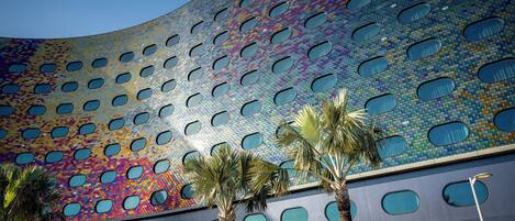 Un edificio moderno con fachada curva que presenta un diseño de mosaico y numerosos ventanales circulares.