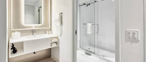 A modern bathroom with a glass-enclosed shower, a large mirror, and a white vanity.