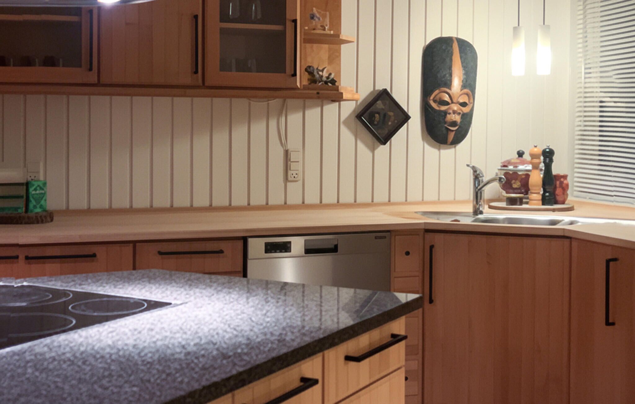 A kitchen with wooden cabinets, a granite countertop, a dishwasher, and a decorative mask on the wall.