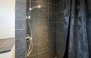 A shower area with dark tiled walls and a showerhead.