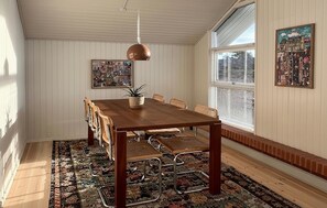 A dining area with a wooden table, metal chairs, a hanging pendant light, and patterned rugs.