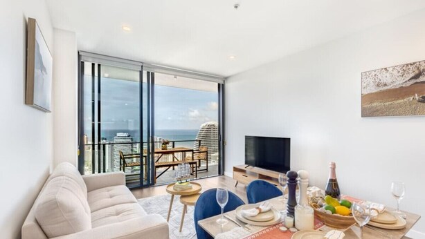 Ein modernes Wohnzimmer mit einer Couch, einem Esstisch für vier Personen und einem Balkon mit Blick auf die Stadt.