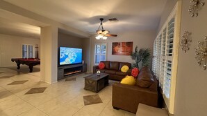 Una sala de estar con mesa de billar, televisor de pantalla plana, ventilador de techo y chimenea.