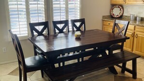 Un comedor con una mesa y sillas de madera oscura, un ventilador de techo y vistas al exterior a través de amplios ventanales.