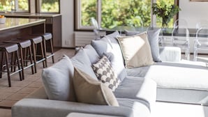 A modern living room with a grey sofa, multiple cushions, a coffee table, and a dining area with bar stools. - Casa La Mount by Elite Havens (Niseko)