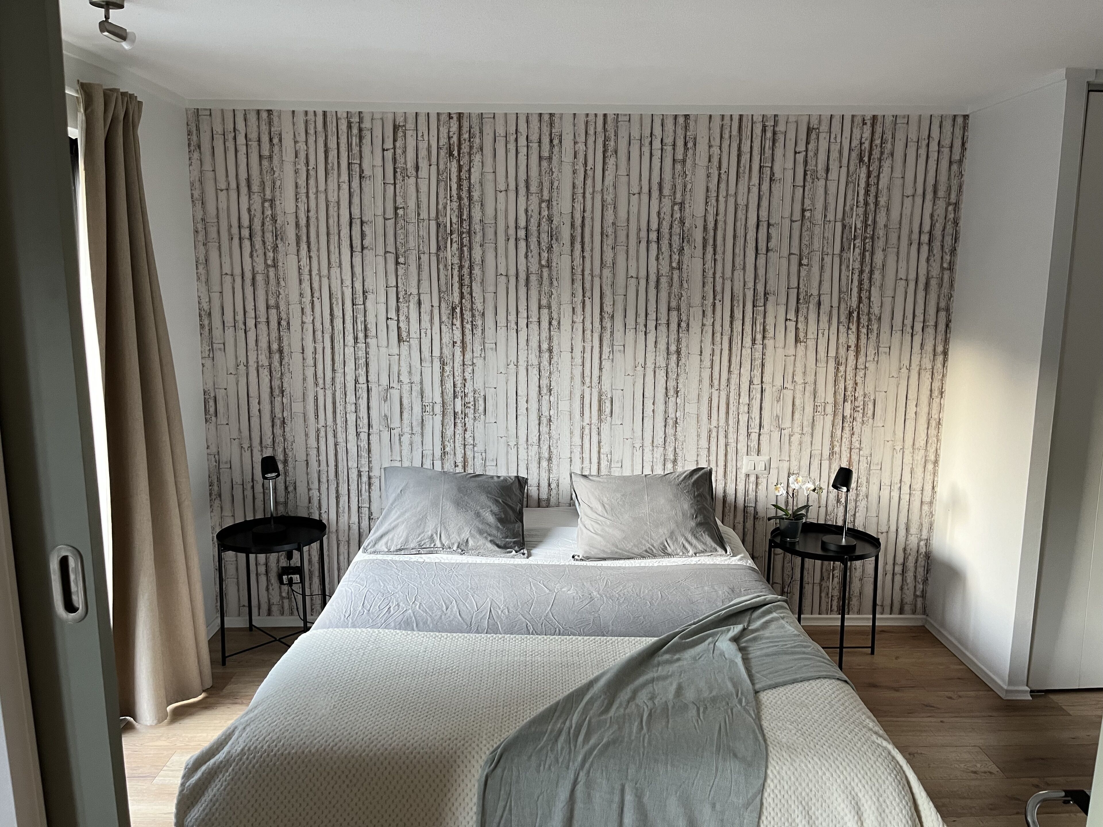 Ein Schlafzimmer mit einem Bett, zwei Nachttischen, einer Lampe und einem Vorhang.