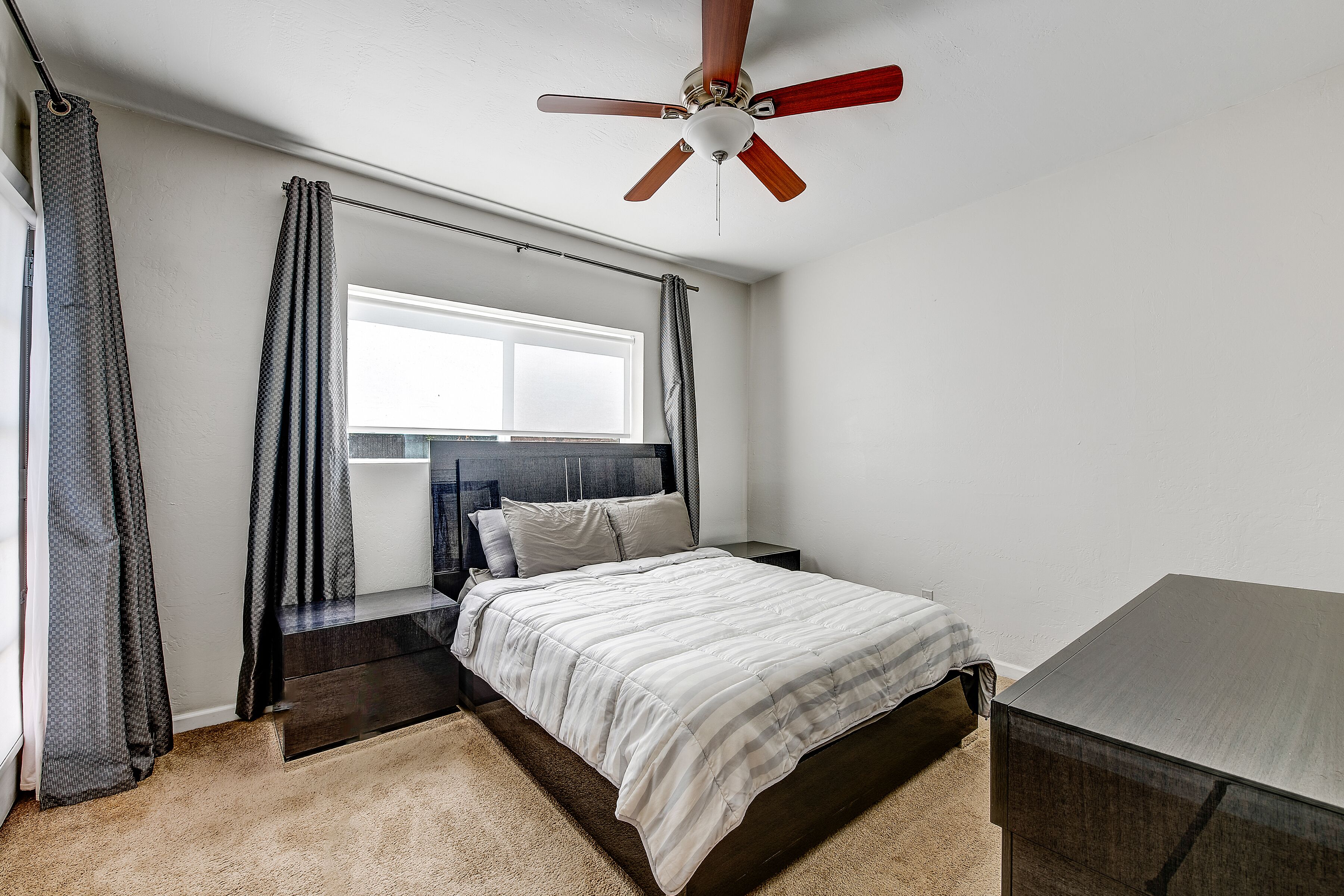 Ein Schlafzimmer mit Bett, Deckenventilator, Fenster und Nachttisch.