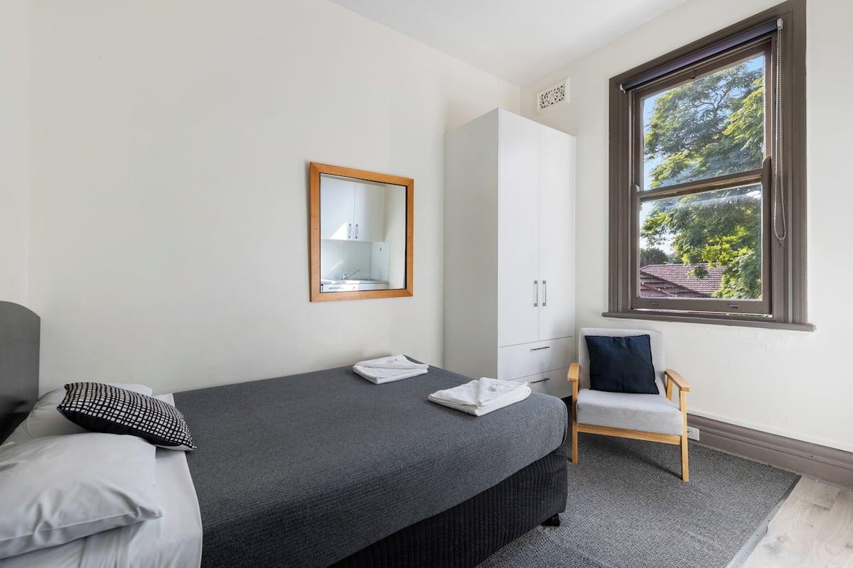 Ein Schlafzimmer mit Bett, Stuhl, Kleiderschrank, Spiegel und einem Fenster mit Blick.