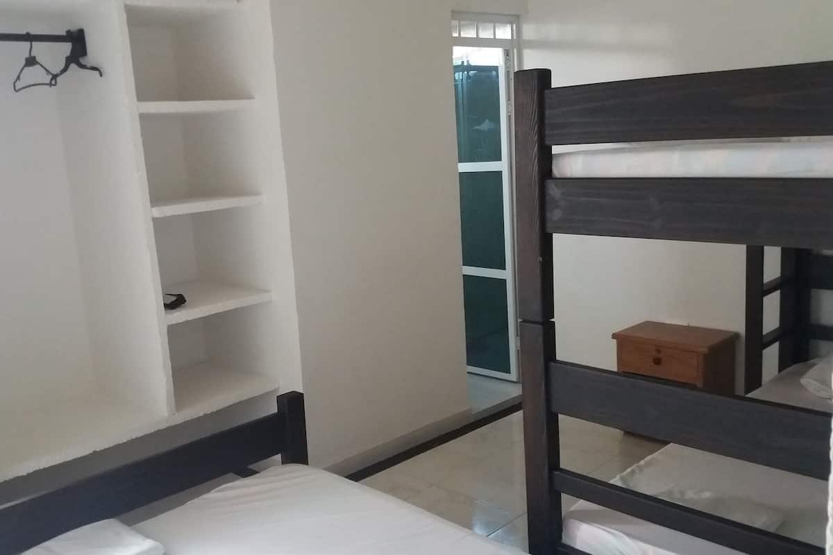 A bunk bed with a wooden frame, a white wall with a shelving unit, and a small wooden box on the bed.