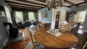 Un salón acogedor con una mesa de comedor de madera, asientos cómodos, un muro de piedra y un área de cocina visible a través de un vano abierto.