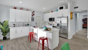A modern kitchen with white cabinets, a central island with stools, a microwave, and a refrigerator. - Sunset Serenity: Your Fort Lauderdale Retreat (Fort Lauderdale)