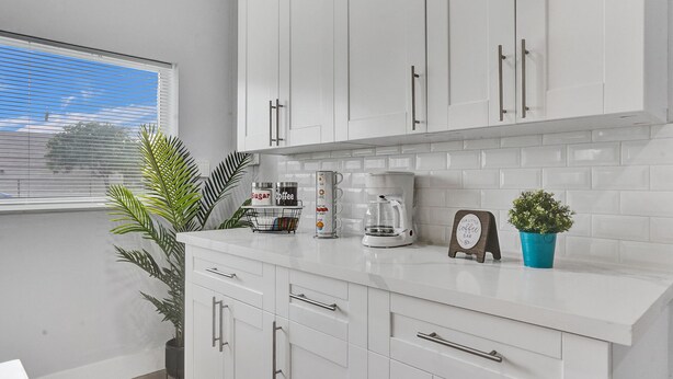A modern kitchen with white cabinets, a coffee maker, and a small clock. - Sunset Serenity: Your Fort Lauderdale Retreat (Fort Lauderdale)
