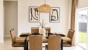 A dining area with a wooden table, six chairs, a vase with branches, and two abstract paintings on the wall.