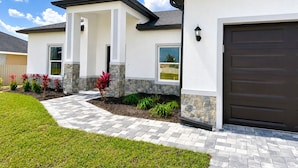 A modern two-story house with a stone accent wall, a driveway with patterned paving, and a dark garage door.