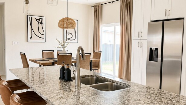 A modern kitchen with a granite countertop, stainless steel appliances, and bar stools.