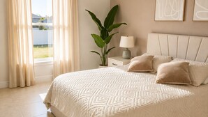 A bedroom with a large bed, a bedside table with a lamp, a potted plant, and artwork on the wall.