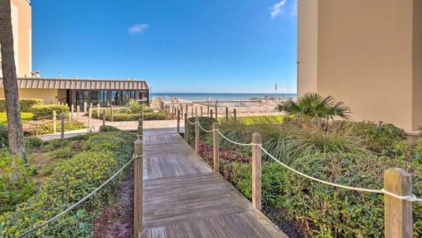A wooden pathway leading to a beach area with a building in the background. - Beachfront on no-drive beach.  Park & walk to local spots.   (New Smyrna Beach)