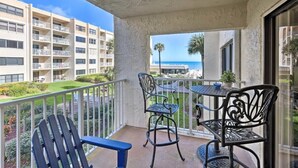 A balcony with a view of a building and the ocean. There are two chairs and a small table. - Beachfront on no-drive beach.  Park & walk to local spots.   (New Smyrna Beach)