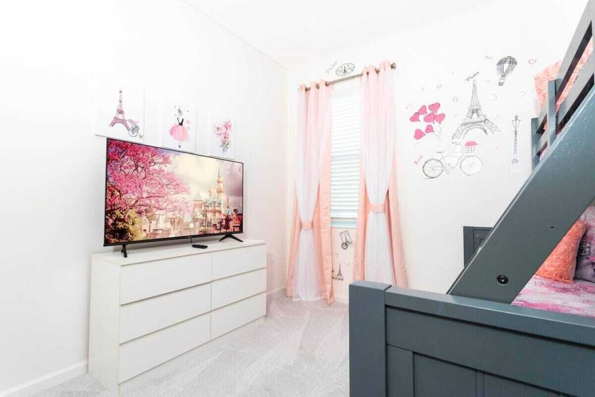 Ein Zimmer mit Fernseher auf einer weißen Kommode, einer Treppe und Wandbildern, darunter der Eiffelturm und Fahrräder.