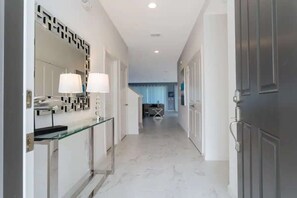 A hallway with a glass partition, a mirror, two lamps, and a door.