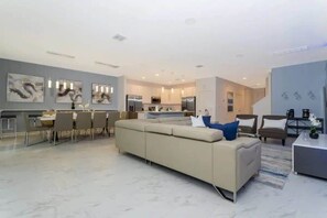 A modern living room with a sofa, dining area, kitchen, and artwork on the walls.