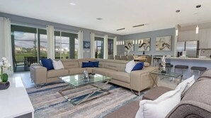 A modern living room with a sectional sofa, a glass coffee table, and a dining area with a kitchen in the background. - 10BD Bella Vida Modern Home Private Pool (BV 4456) (Kissimmee)