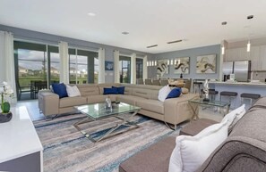 A modern living room with a sectional sofa, a glass coffee table, and a dining area with a kitchen in the background.
