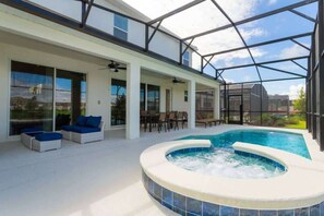 A modern indoor pool area with a hot tub, lounge chairs, and a glass-enclosed patio.