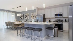 A modern kitchen with a central island, bar stools, stainless steel appliances, and a dining area with chairs and a table. - 10BD Bella Vida Modern Home Private Pool (BV 4456) (Kissimmee)