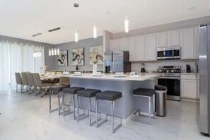 A modern kitchen with a central island, bar stools, stainless steel appliances, and a dining area with chairs and a table.